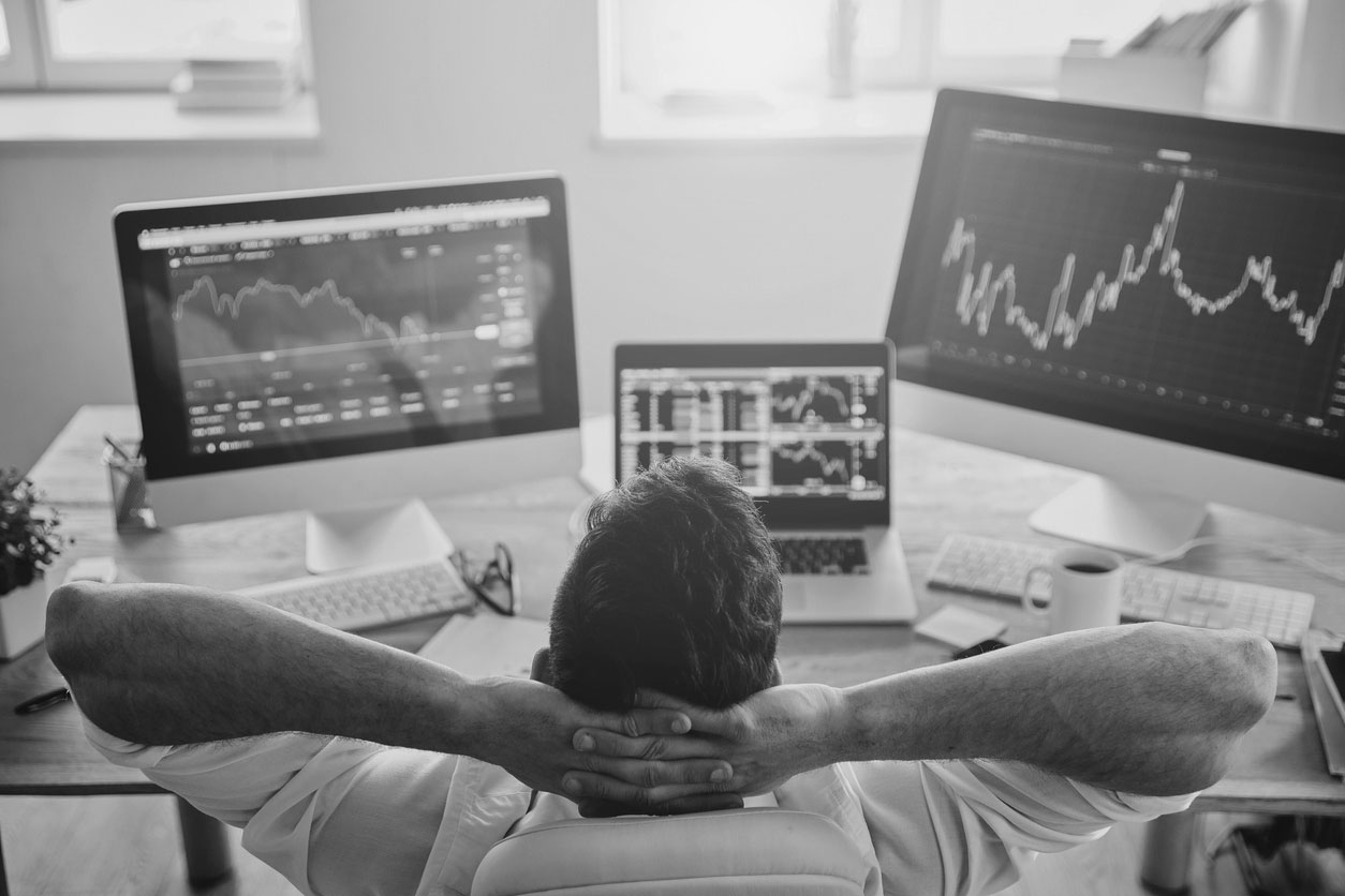 man sitting back and looking at three computer screens.